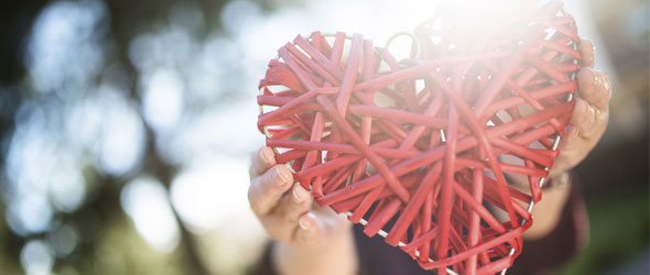 Heart made from wood strips being held up with two hands outside