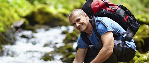 Young man hiking near a stream and smiling at the camera