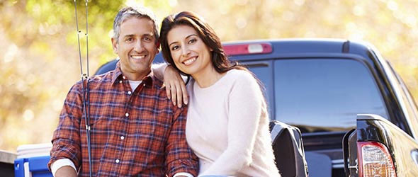 Young couple sitting on the back of a truck and smiling at camera