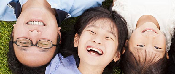 Dad and two kids laying on grass and smiling at camera