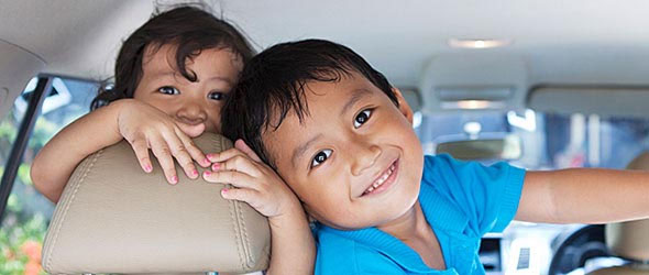 Two young children in back seat of car looking at camera smiling
